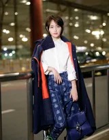 张嘉倪侧身回眸，米色大衣如披风般飘逸，身后霓虹灯光晕染开一片梦幻光斑