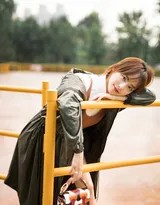 她惬意地坐在公园长椅上，双臂舒展搭着椅背，仰头感受微风，笑容里满是自在与放松