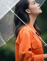 李沁身着橘色工装外套，手持透明雨伞，在雨中的森林小径上惬意漫步，发丝微湿，笑容清新