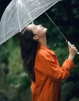 李沁倚靠木栏侧身回眸，透明雨伞倚在肩头，眼神温柔略带笑意，身后的森林因雨水而显得更加深邃静谧