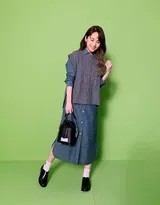 杨丞琳倚靠墙壁，身穿牛仔背带裤搭配条纹衫，笑容灿烂如春日暖阳