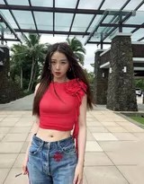 虞书欣倚靠于简洁墙面，红色上衣与浅色背景形成鲜明对比，她直视镜头眼神自信而略带俏皮