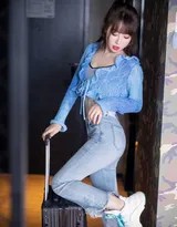 電競藍光下，身著天藍色針織上衣與深藍緊身牛仔褲的長髮模特，側身倚靠電競椅，修長雙腿線條一覽無遺，冷艷眼神直視鏡頭