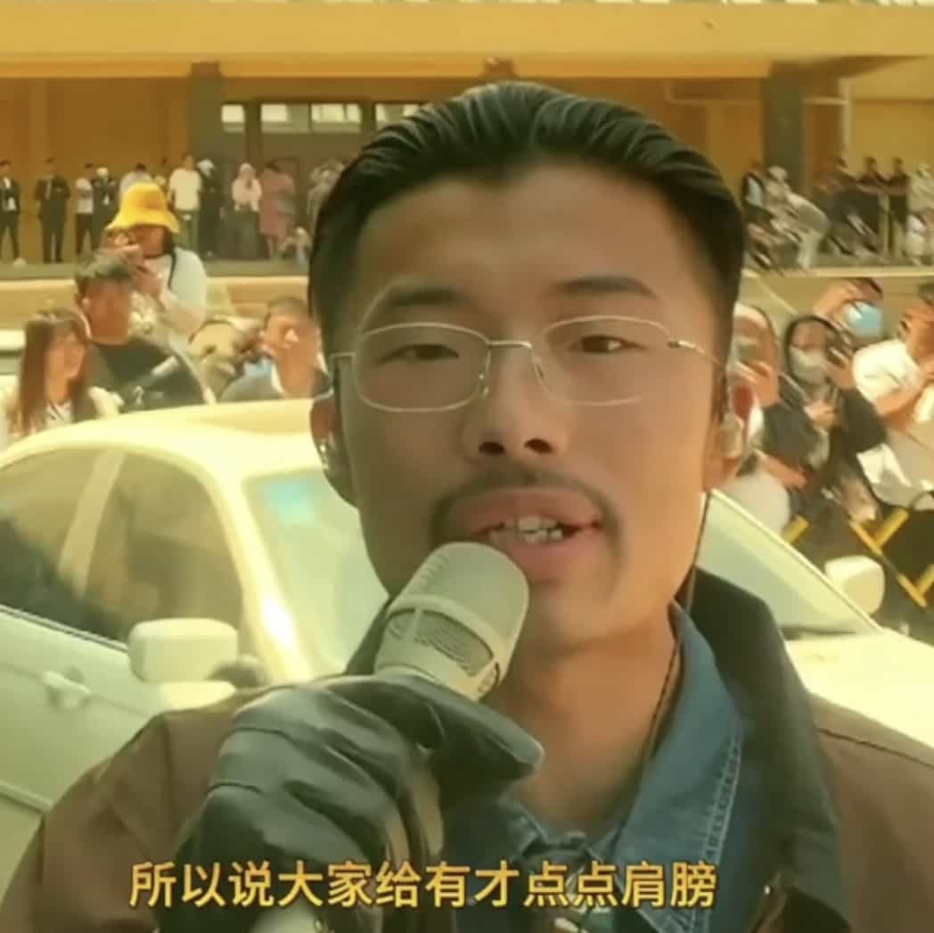 郭有才在菏泽南站前深情演唱，他身穿复古西装，神情专注，身后是见证时代变迁的老车站建筑，面前众多手机记录着这一动人场景。