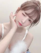 暖光灯下，女孩身穿酒红色毛绒吊带，轻托脸颊对镜甜笑，蓬松丸子头与纤细锁骨构成可爱又性感的画面