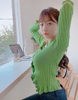 少女侧身倚靠窗前，绿色衣裙与窗外绿植相映成趣