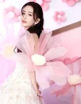 佟丽娅轻倚花枝，眼眸低垂似含露，纱裙裙摆铺展如盛放之莲