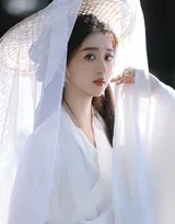 美人回眸，手持长剑立于青草坡上，身后湖面辽阔，眼神中带着一丝探寻与故事感。