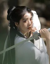 长剑横于身前，李凯馨凝视剑身，湖畔微风拂动她的长发与飘带，意境深远。