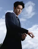 王鹤棣身着白色西装凝视远方，海浪轻抚沙滩，落日余晖洒在肩头