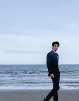 侧身立于浅滩，海水浸湿裤脚，他低头沉思，潮湿的刘海垂下，尽显静谧与故事感