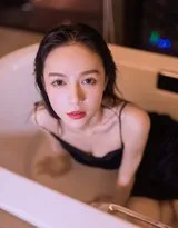 氤氲水汽中，身着黑色丝质吊带裙的女子慵懒倚靠，水珠如钻石般缀于锁骨与裙边，昏黄灯光为其轮廓镀上一层温暖光晕。