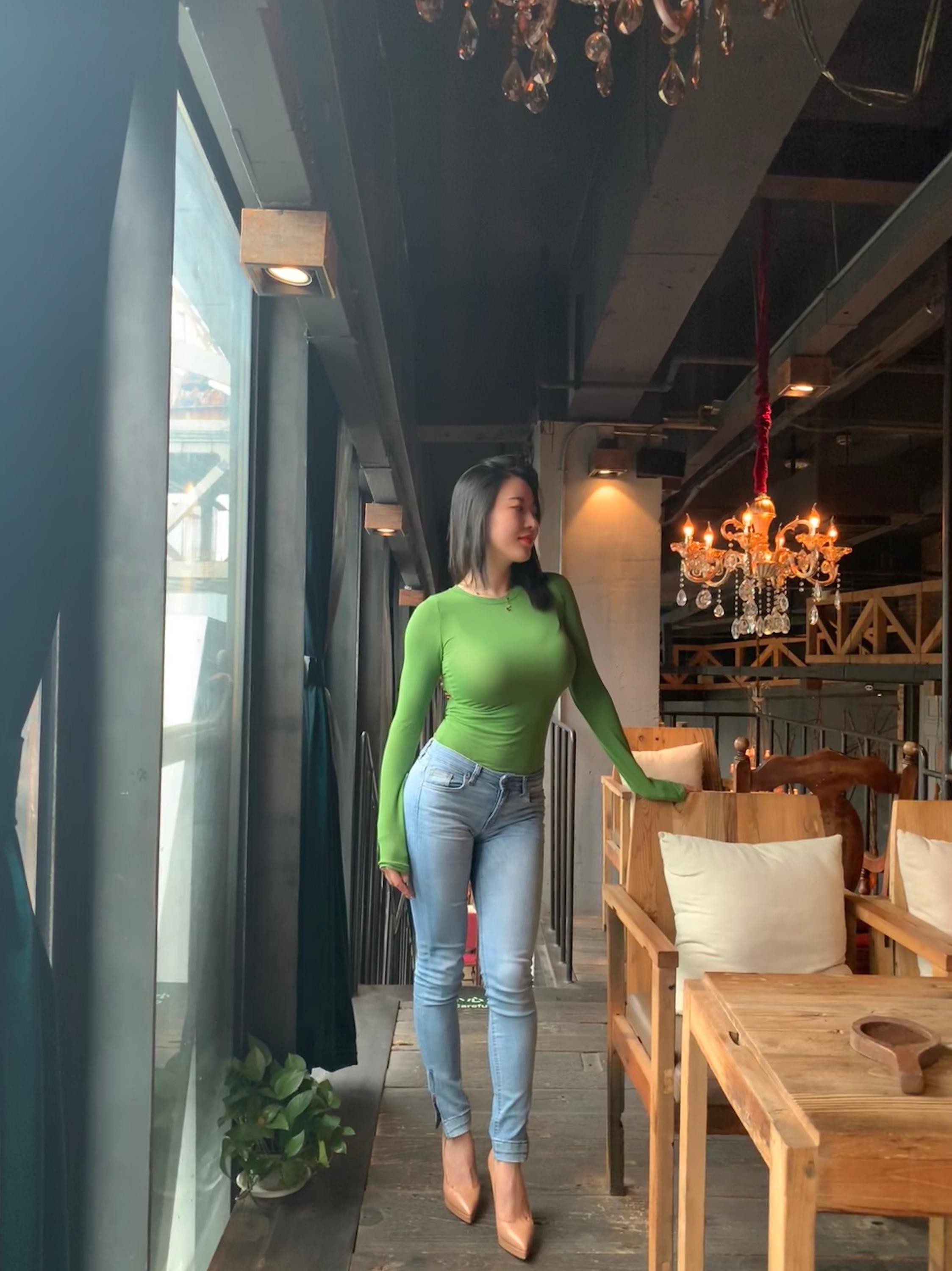 女性着深色内衣与牛仔裤倚靠墙边，展现性感健康体态