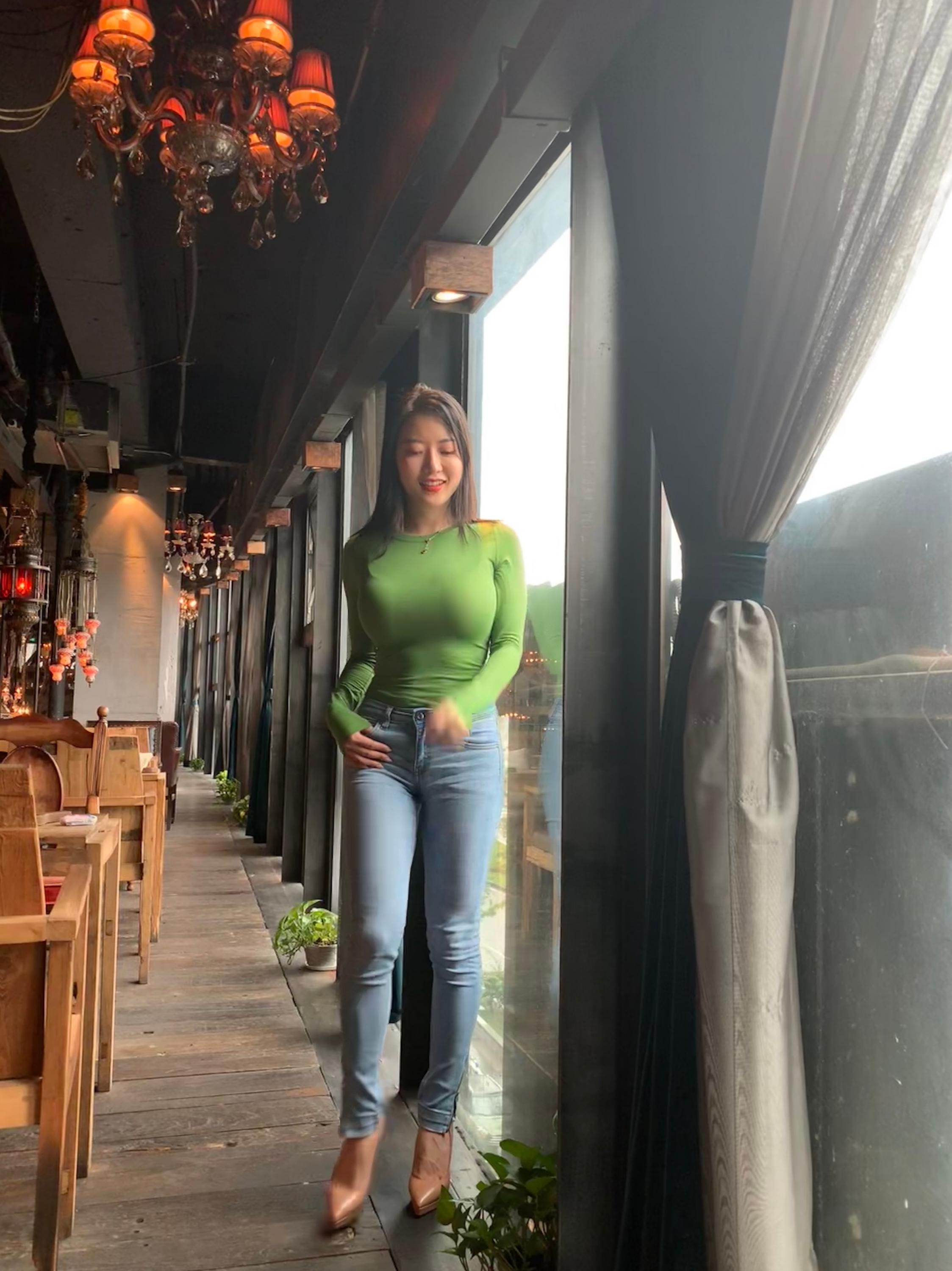 女性以牛仔裤搭配露肩上衣，坐姿展现优雅与性感并存的气质