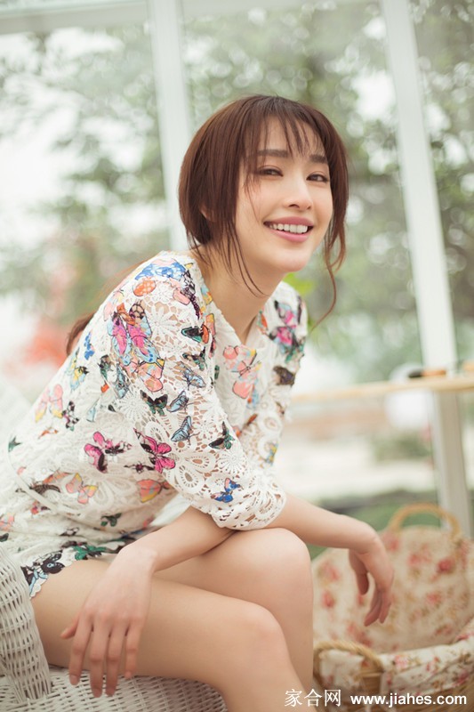 张俪低头浅笑，手抚花枝，午后阳光为她周身镀上了一层温暖光晕