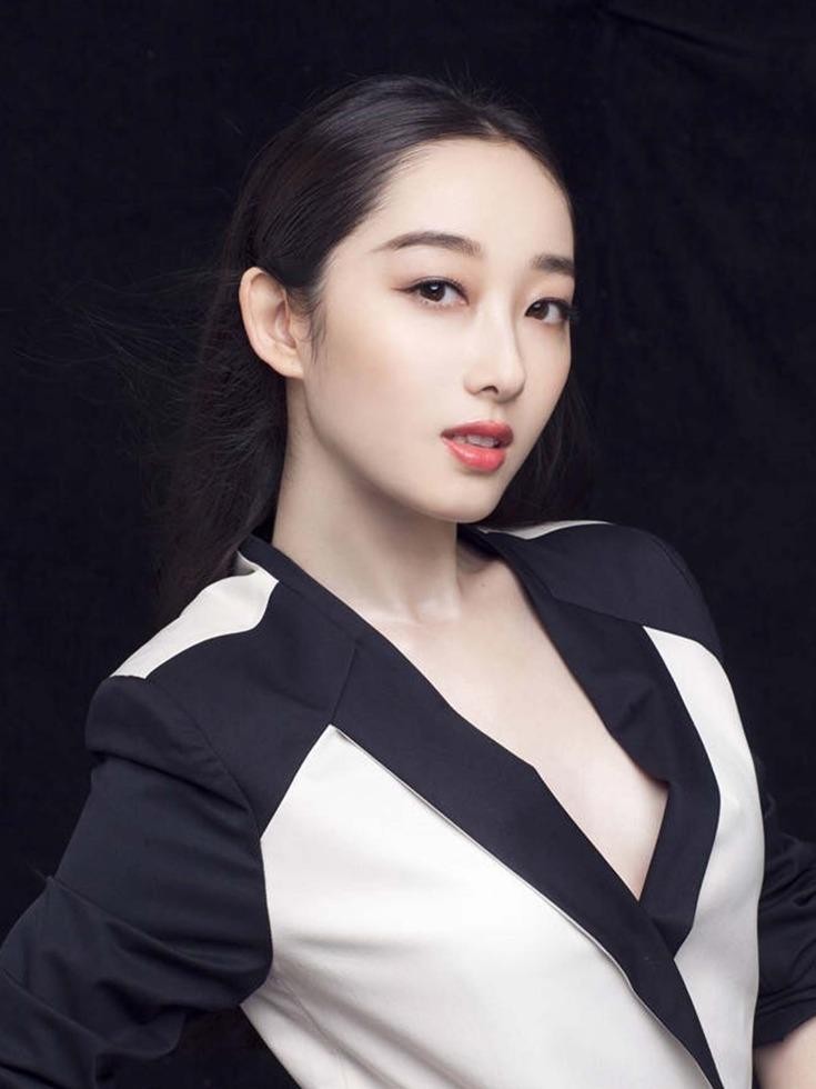 蒋梦婕一袭简约绸裙立于暗调背景中，双臂轻环，下颌微扬，展现清冷而自信的都市女性魅力