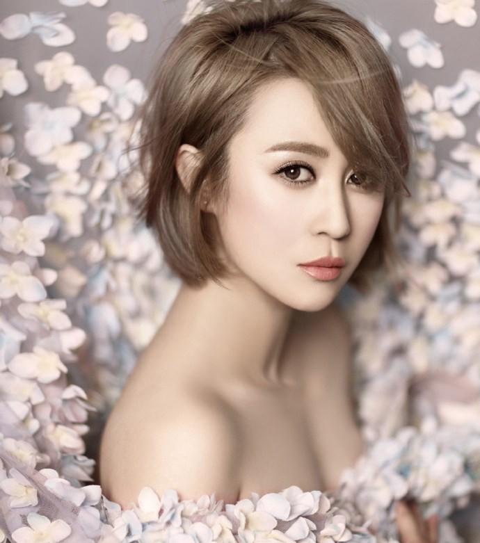 马丽身着花瓣长裙侧坐花丛，眼神温柔眺望远方，宛如花中仙子